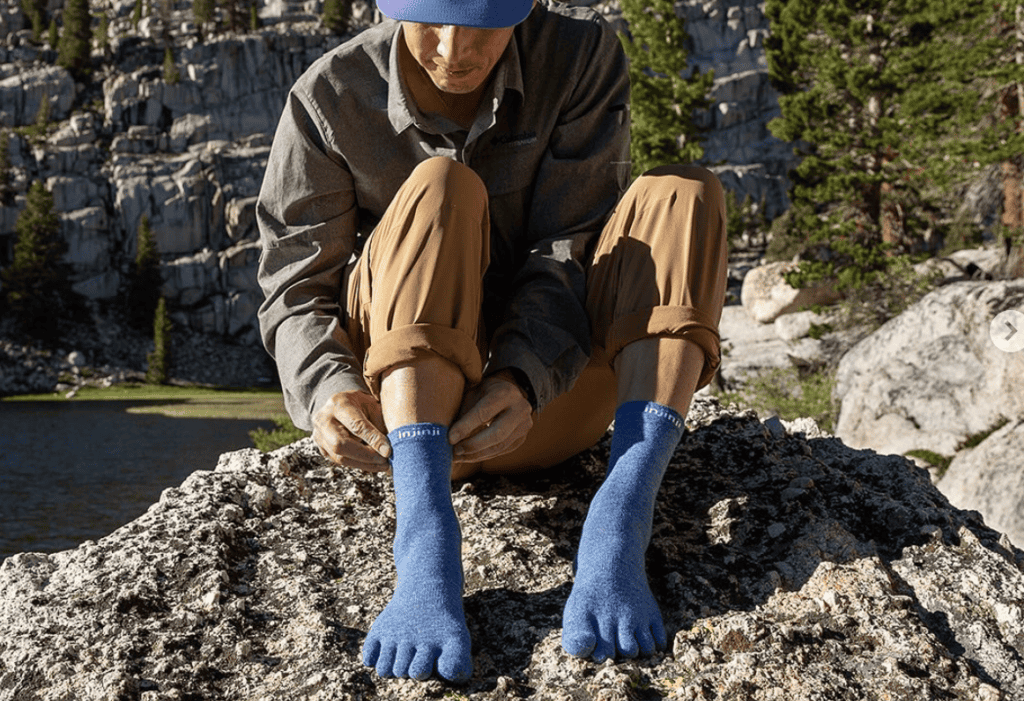 woman sitting on a rock by a lake putting on a pair of blue toe socks